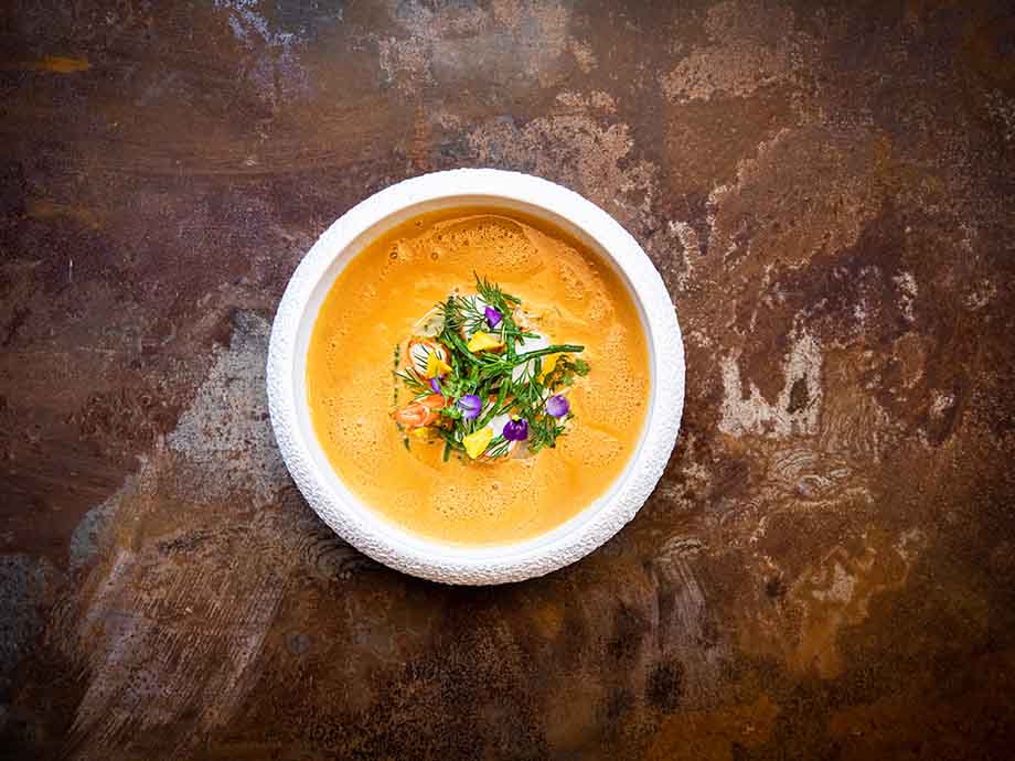 Riesengarnelen Bisque. Auf einem weissen Teller mit dünnem Rand angerichtet. Dekoriert mit buntem wildkräutersalat und frischem Dill.