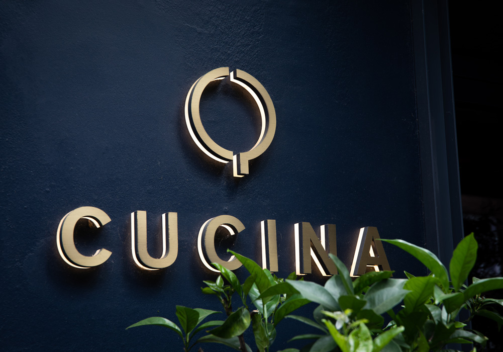 cooking sign, cucina sign, gold letters, blue wall, plant foreground